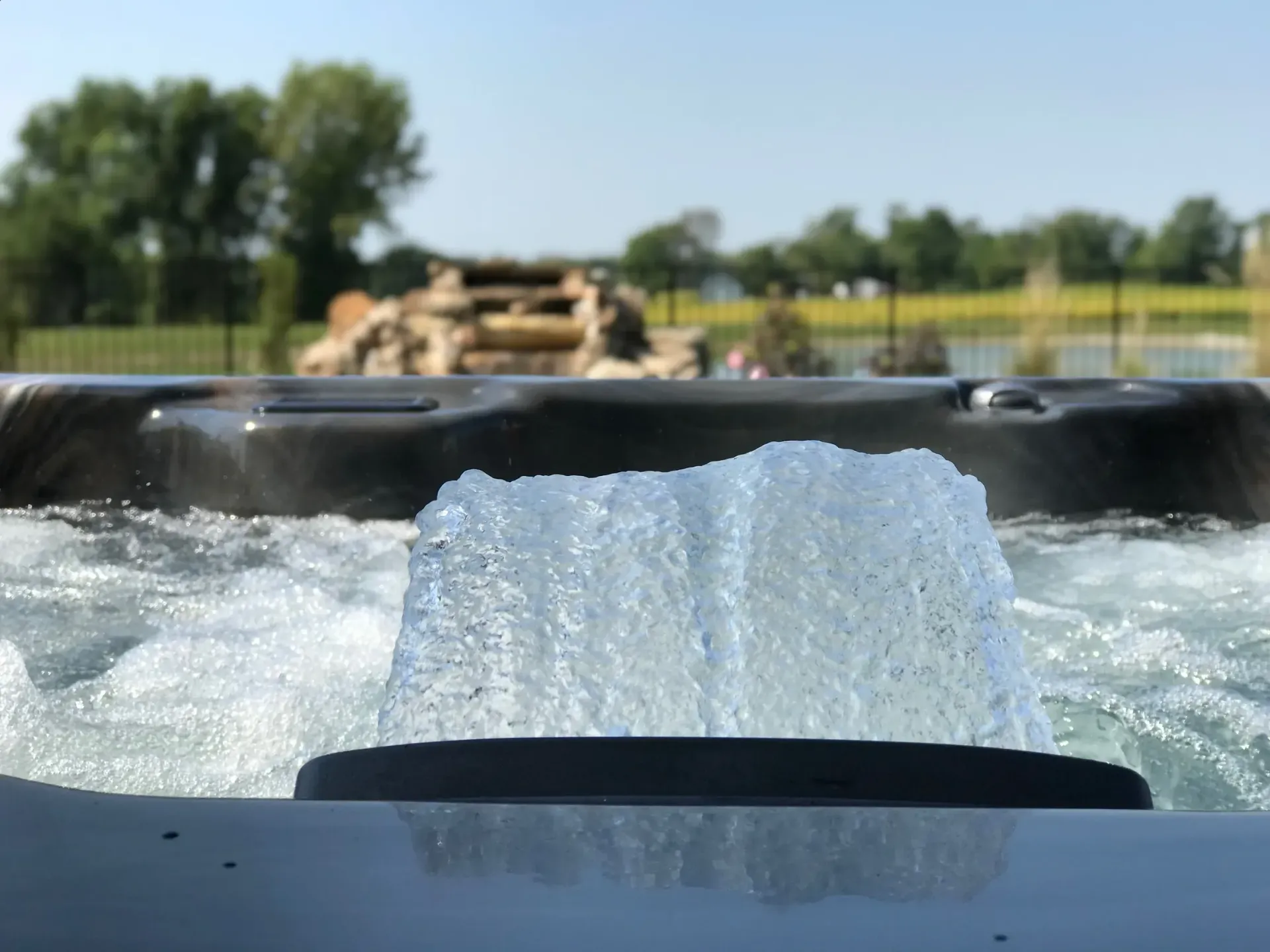 Bubbling hot tub jets; blurred background of a sunny outdoor setting with a waterfall feature.