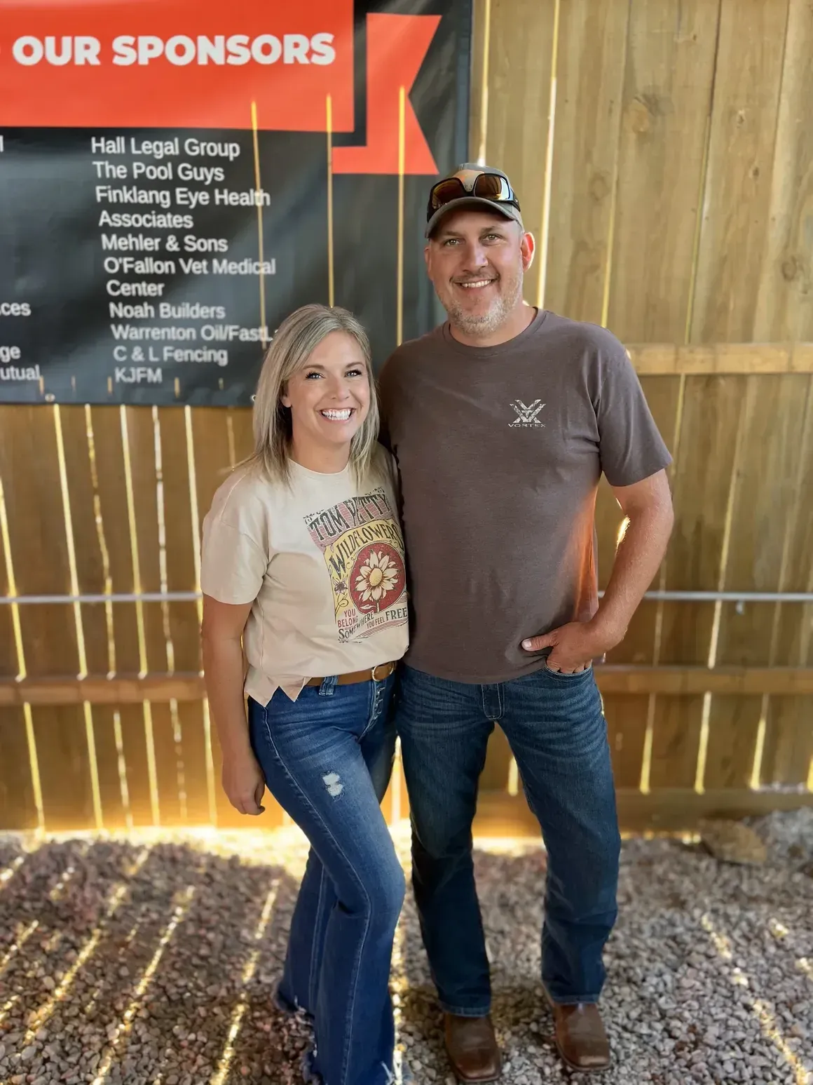 Woman and man standing together in front of a sign; woman is smiling, man has his hand in pocket.