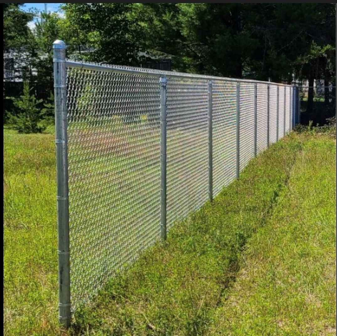 Chain link fence in a grassy area, with trees in the background.