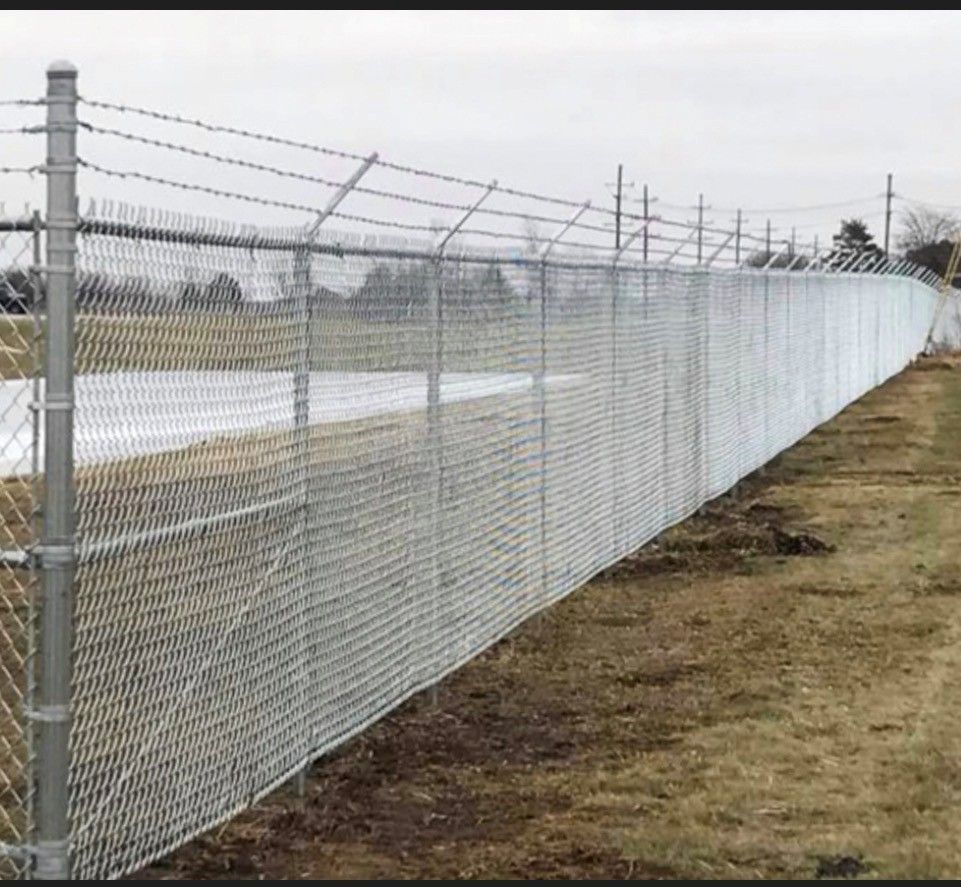 Chain link fence topped with barbed wire, surrounding an outdoor area with a brown field.