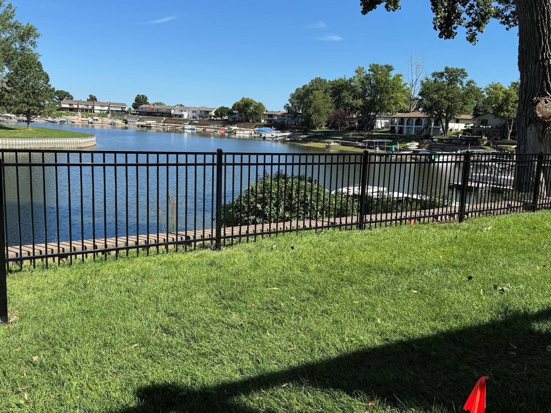 Black metal fence with a lake and houses in the background on a sunny day.