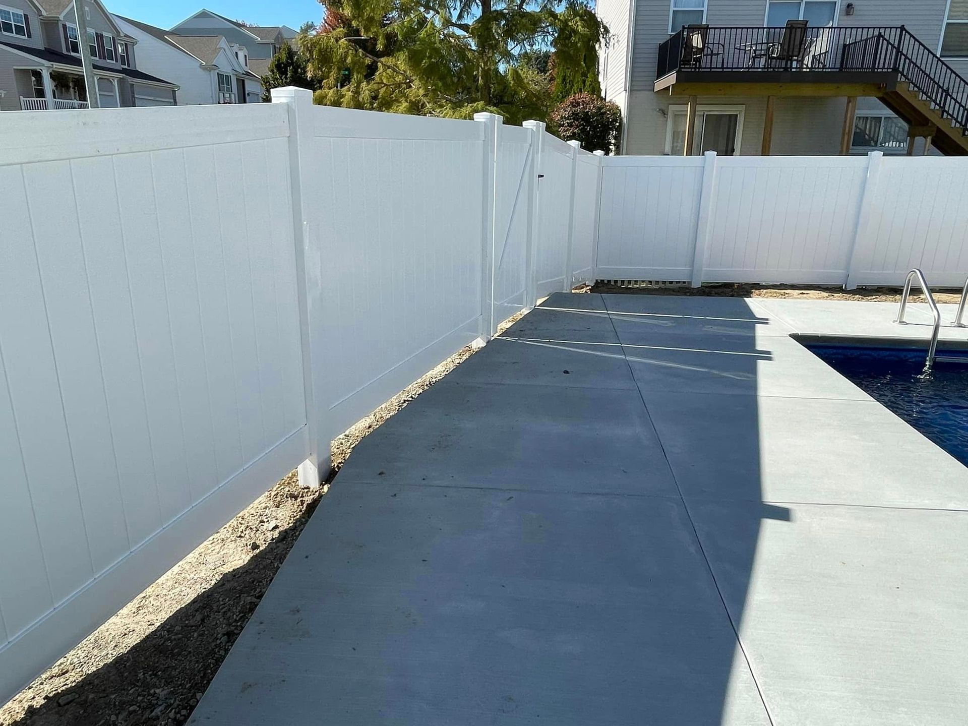 a white fence surrounds a swimming pool with a house in the background