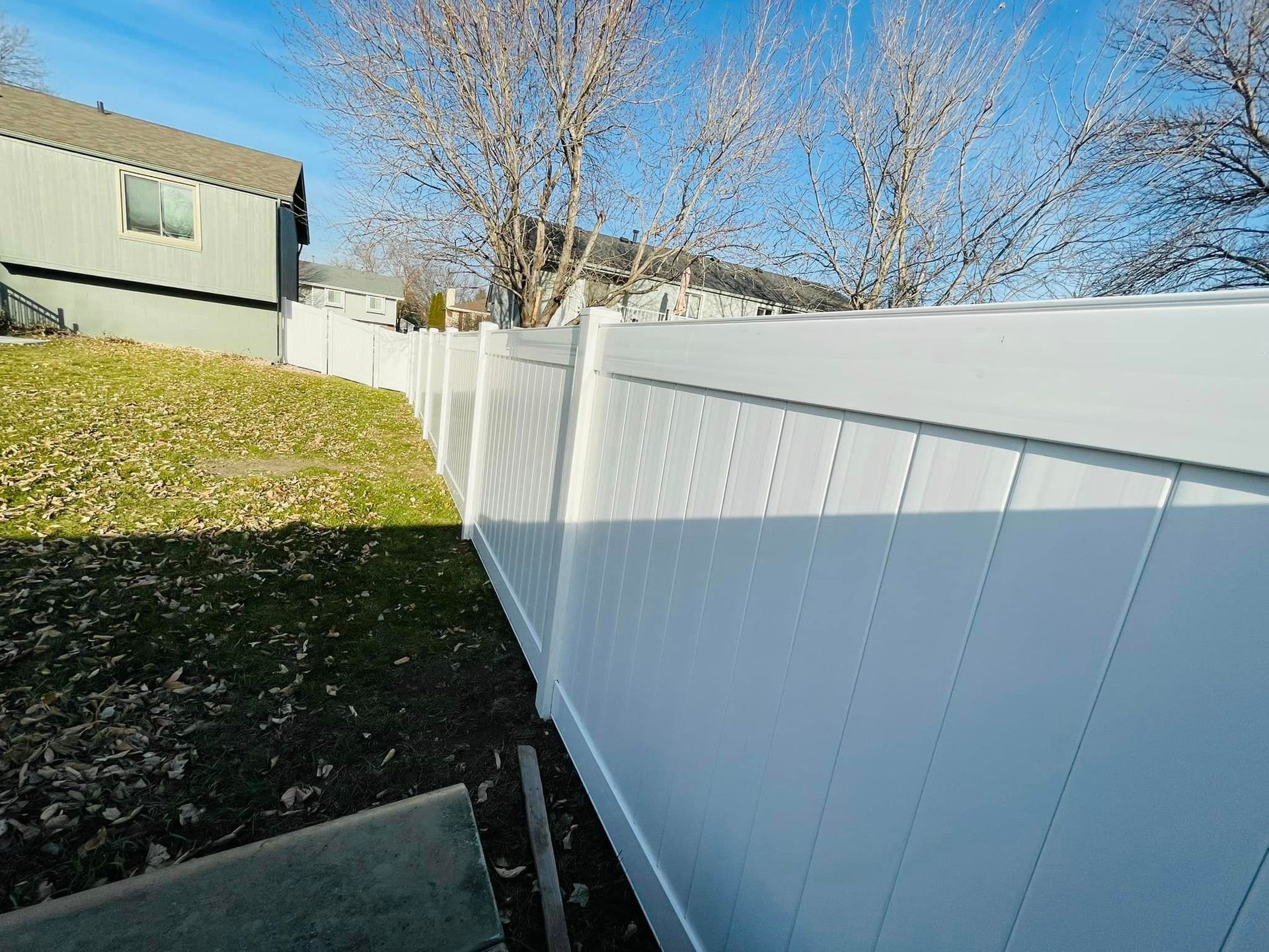 a white fence surrounds a yard with dried leaves