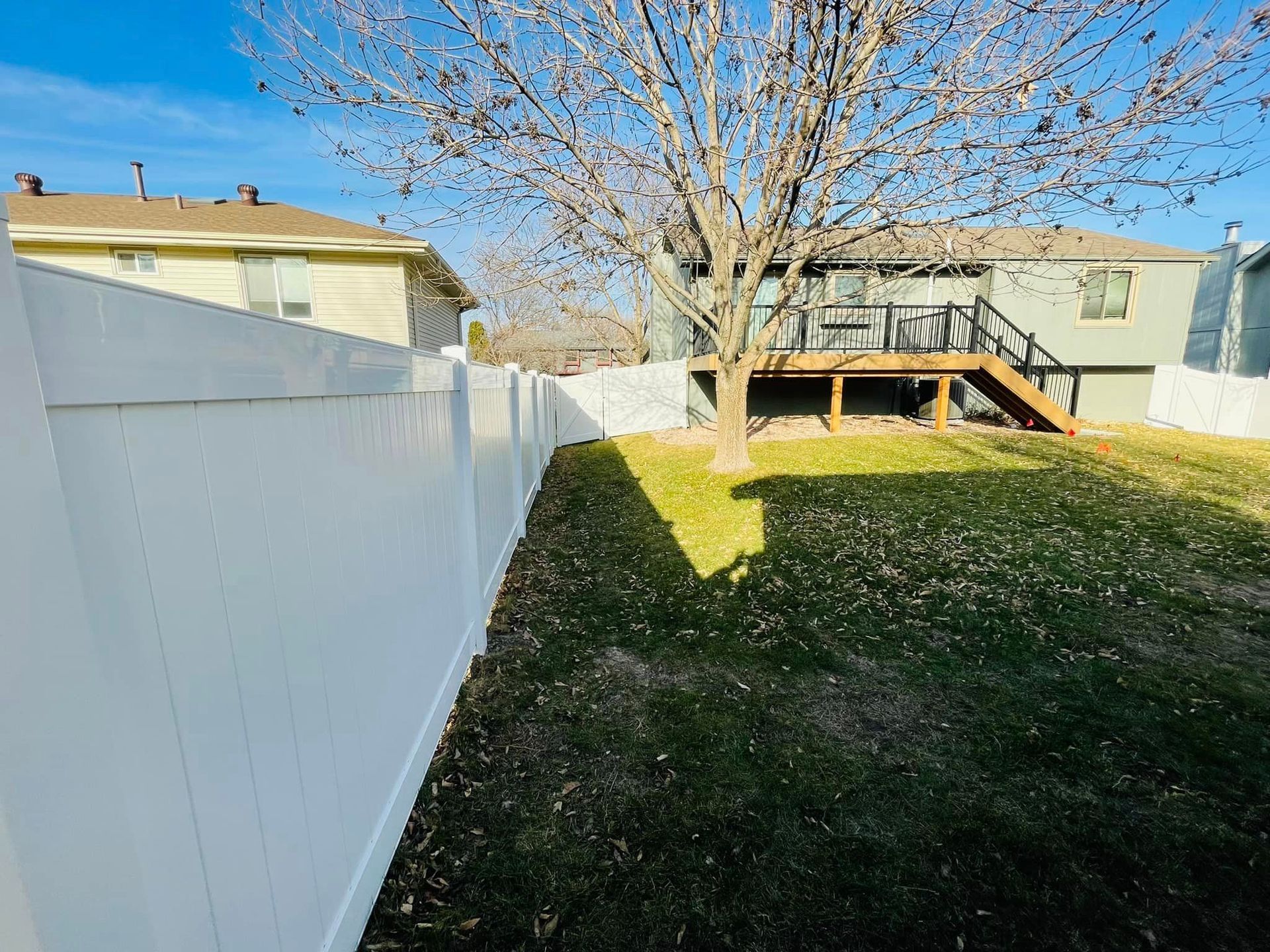a white fence surrounds the backyard of a house with a huge tree