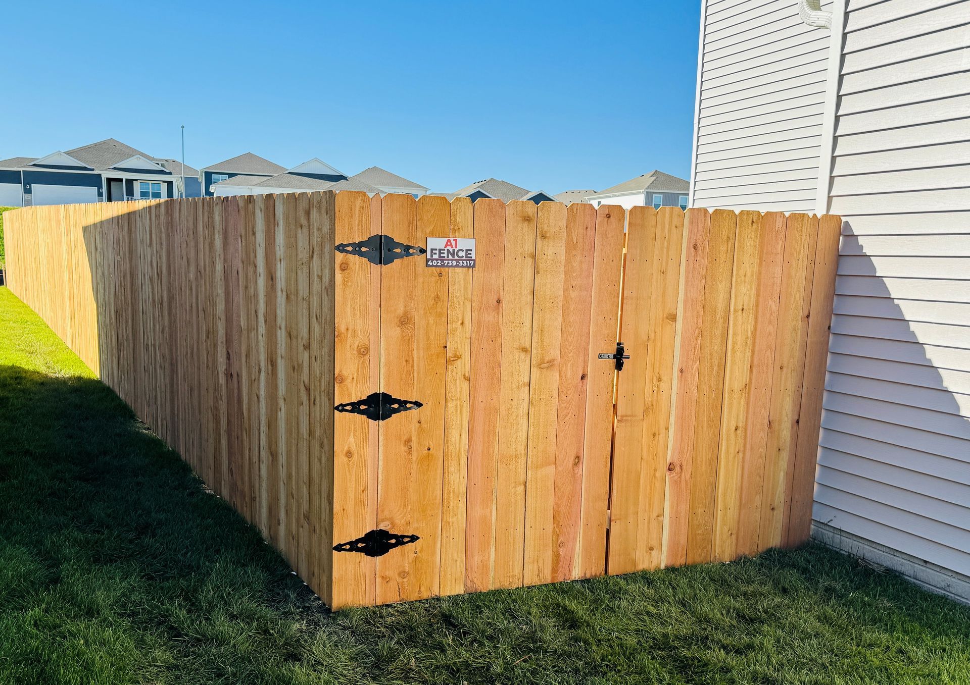 Wooden fence with black hinges, next to a white house, under a blue sky.