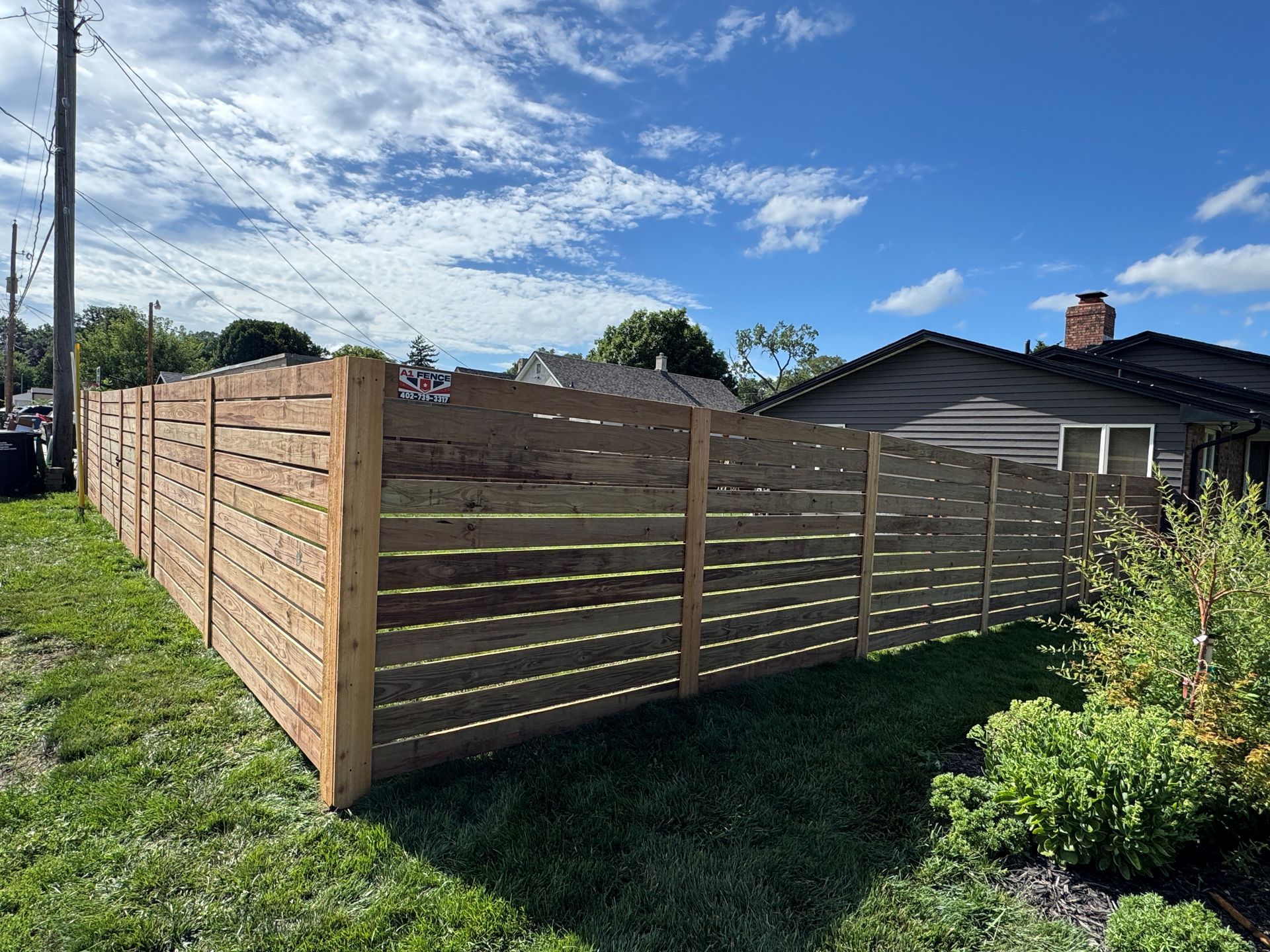 Wooden horizontal slat fence in a yard, sunny day.
