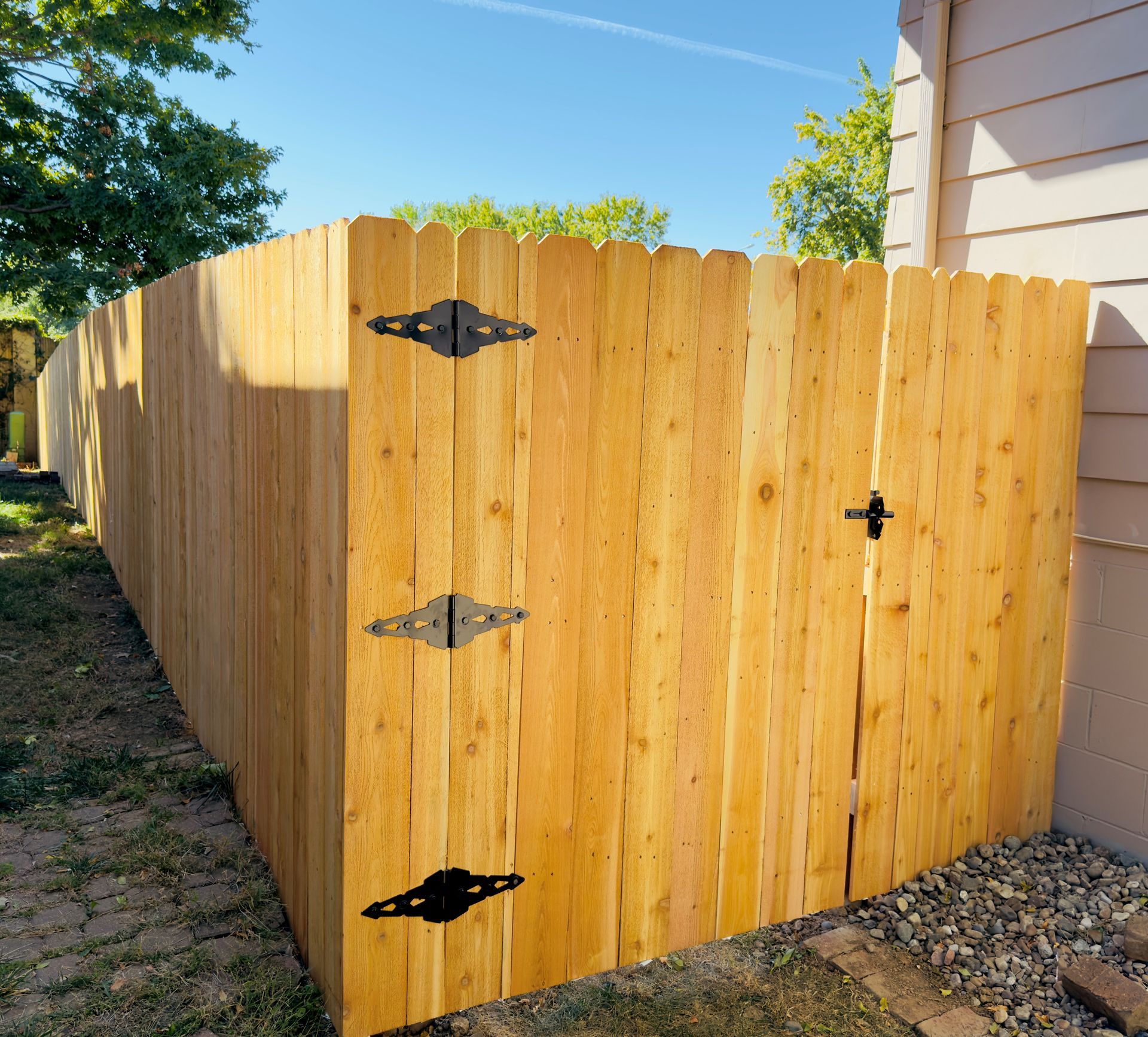 Wooden fence with a gate, attached to a house. Black hinges and latch.