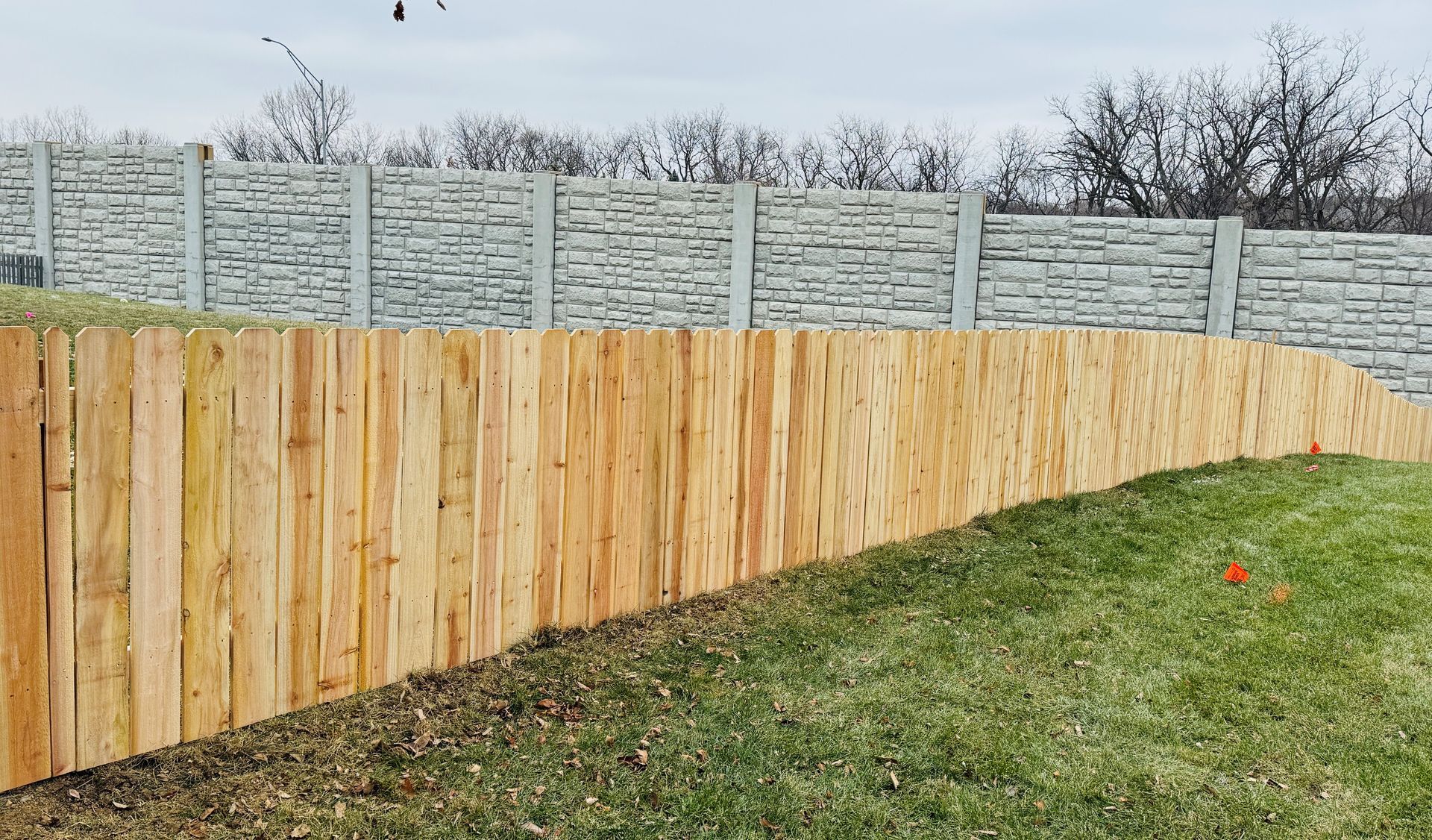 Wooden fence curving on a grassy hill, with a stone wall in the background under a cloudy sky.