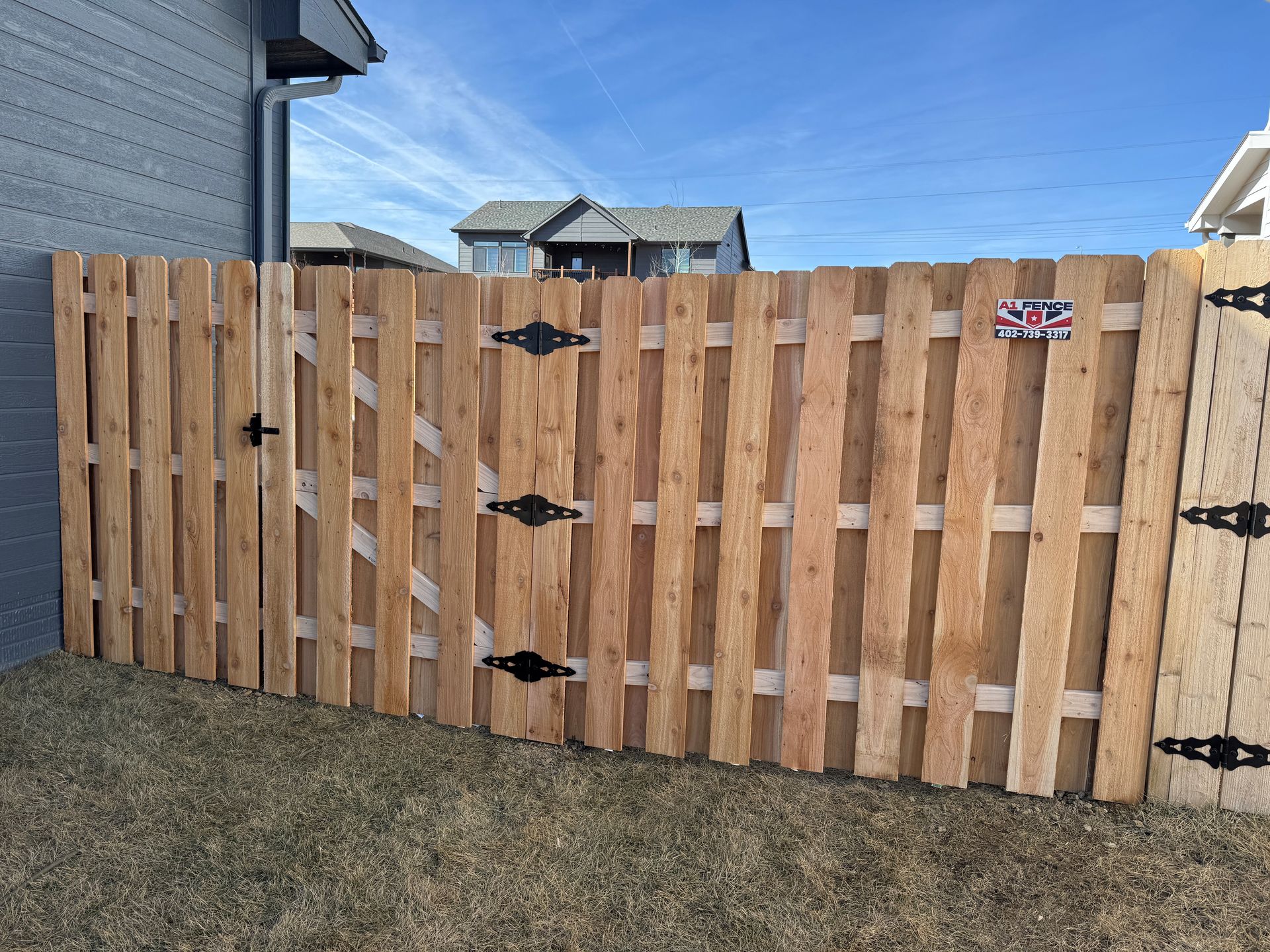 Wooden fence with gate, black hinges, and a small sign in an outdoor setting.