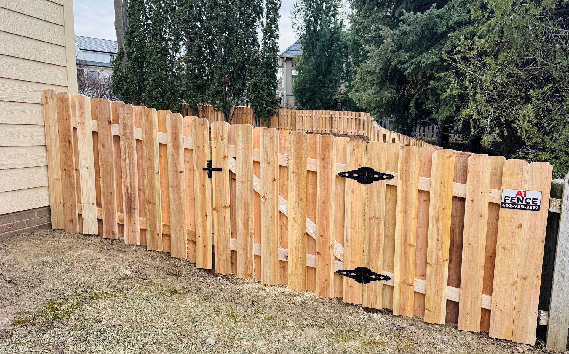 Wooden fence with gate, enclosing a yard with green grass and trees.