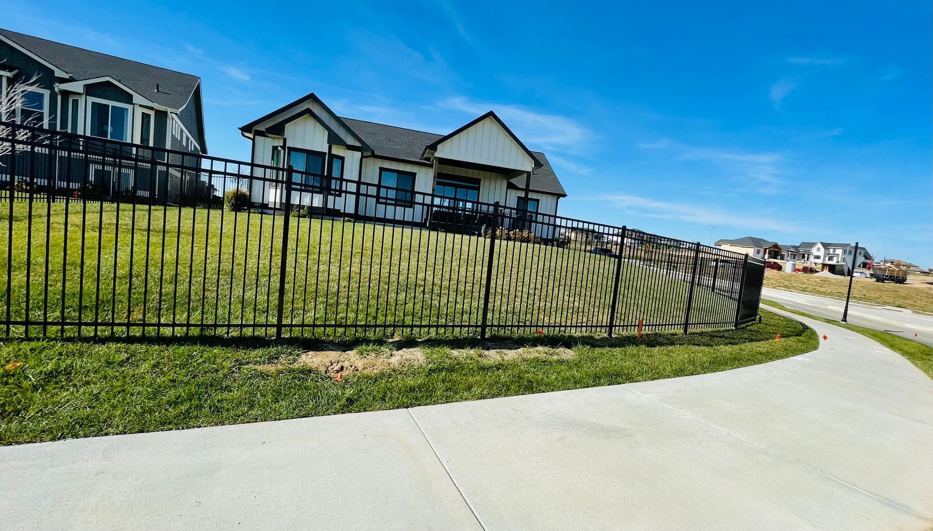 Black metal fence with privacy screen in front of a house, next to a sidewalk, on a sunny day.