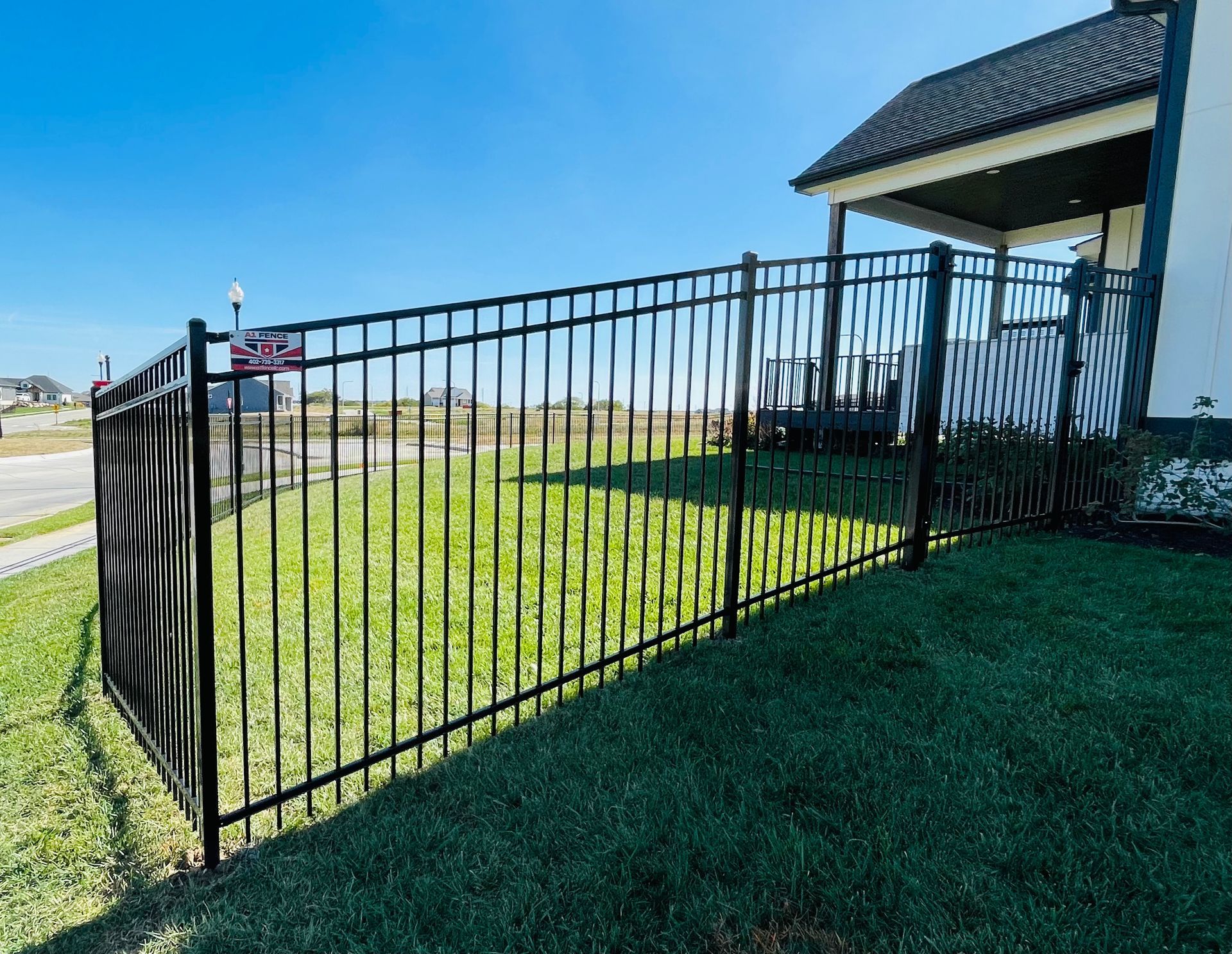Black metal fence enclosing a grassy yard next to a house on a sunny day.