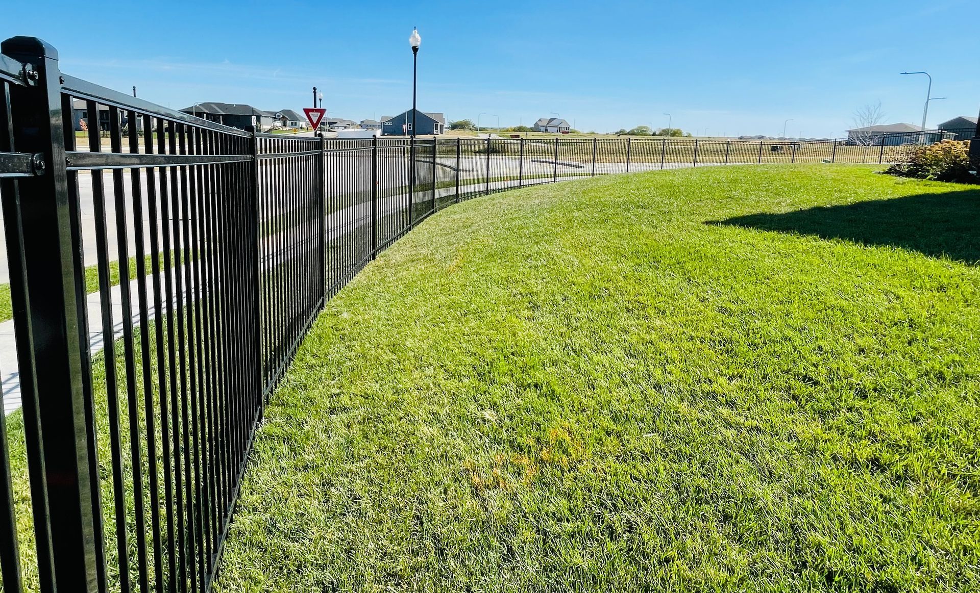 Black metal fence bordering a green lawn on a sunny day.