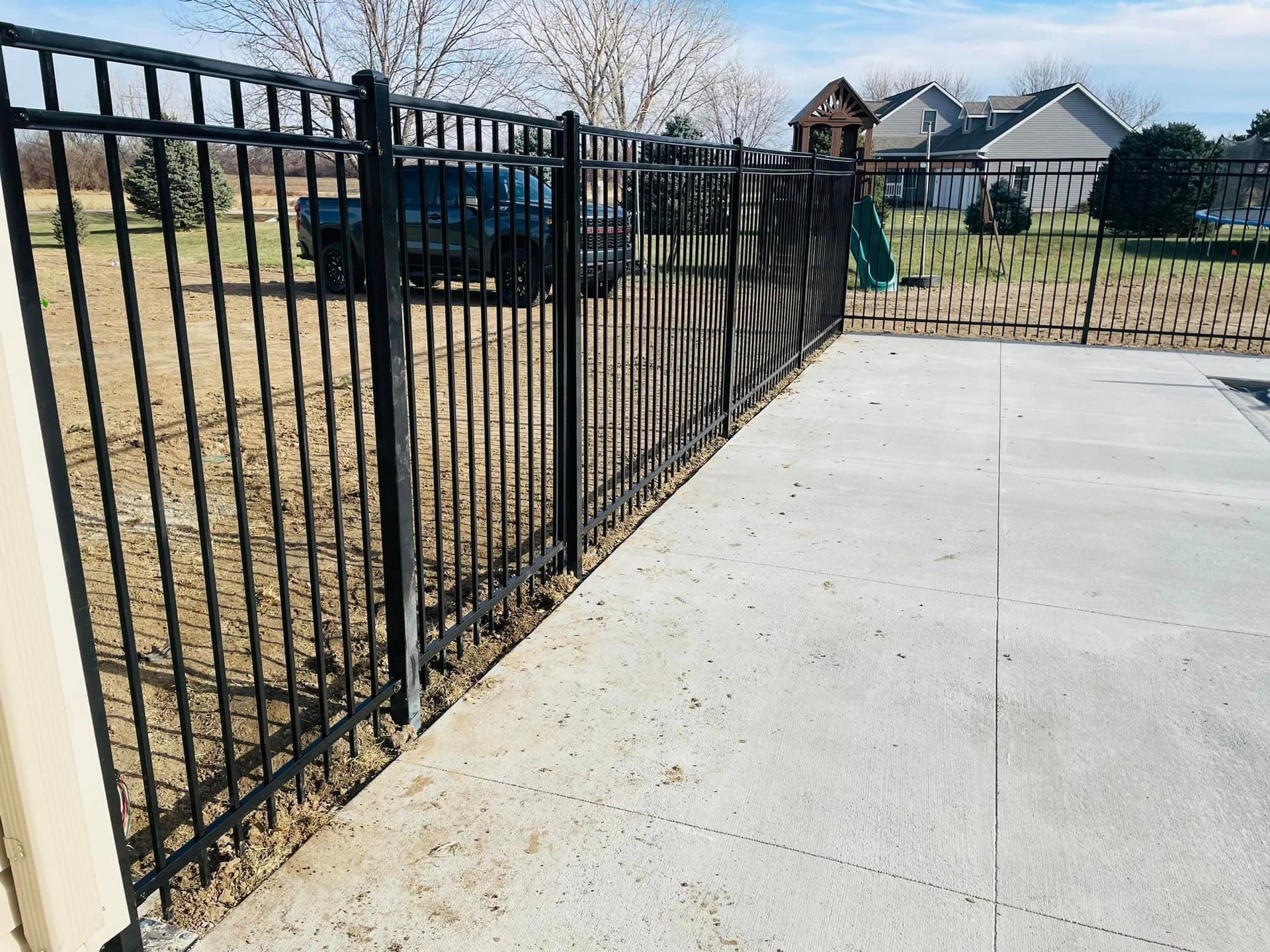 Black metal fence surrounds a concrete patio next to a grassy yard.
