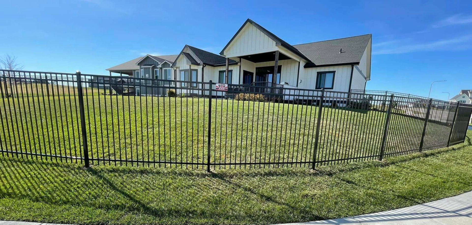 Black fenced yard surrounds white house with black roof, under blue sky.