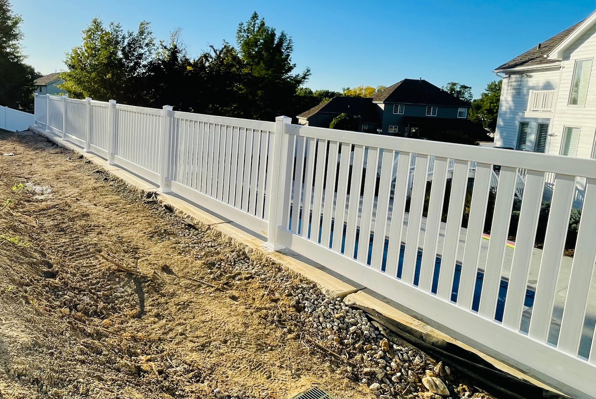 White picket fence with decorative panels, along a dirt path, sunny day.