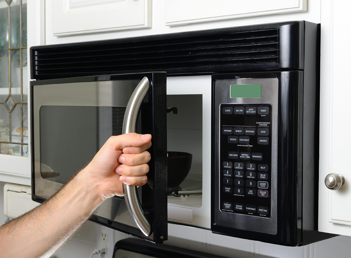 A person is opening a microwave in a kitchen.