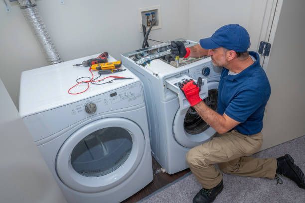 A man is fixing a washer and dryer in a laundry room.