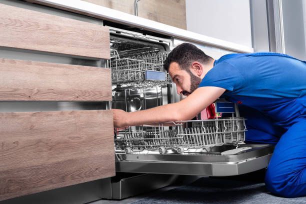 A man is fixing a dishwasher in a kitchen.