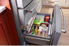 A refrigerator with a drawer filled with food in a kitchen.