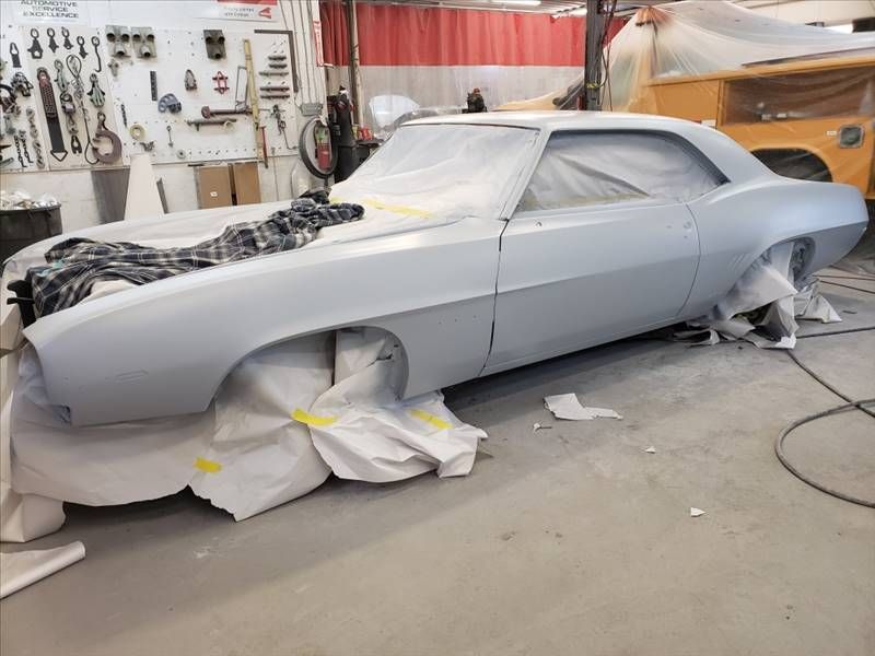 Gray classic car body in a workshop, masked and primed for painting, surrounded by tools and equipment