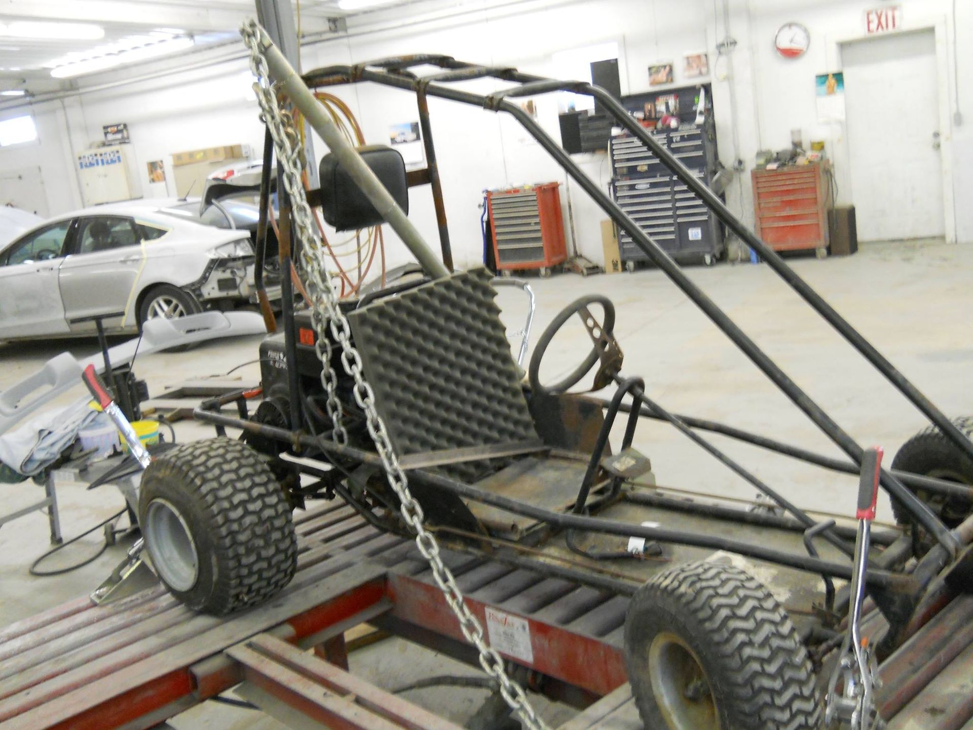 Custom-built buggy frame in an auto shop, with large tires and exposed roll cage on a lift system