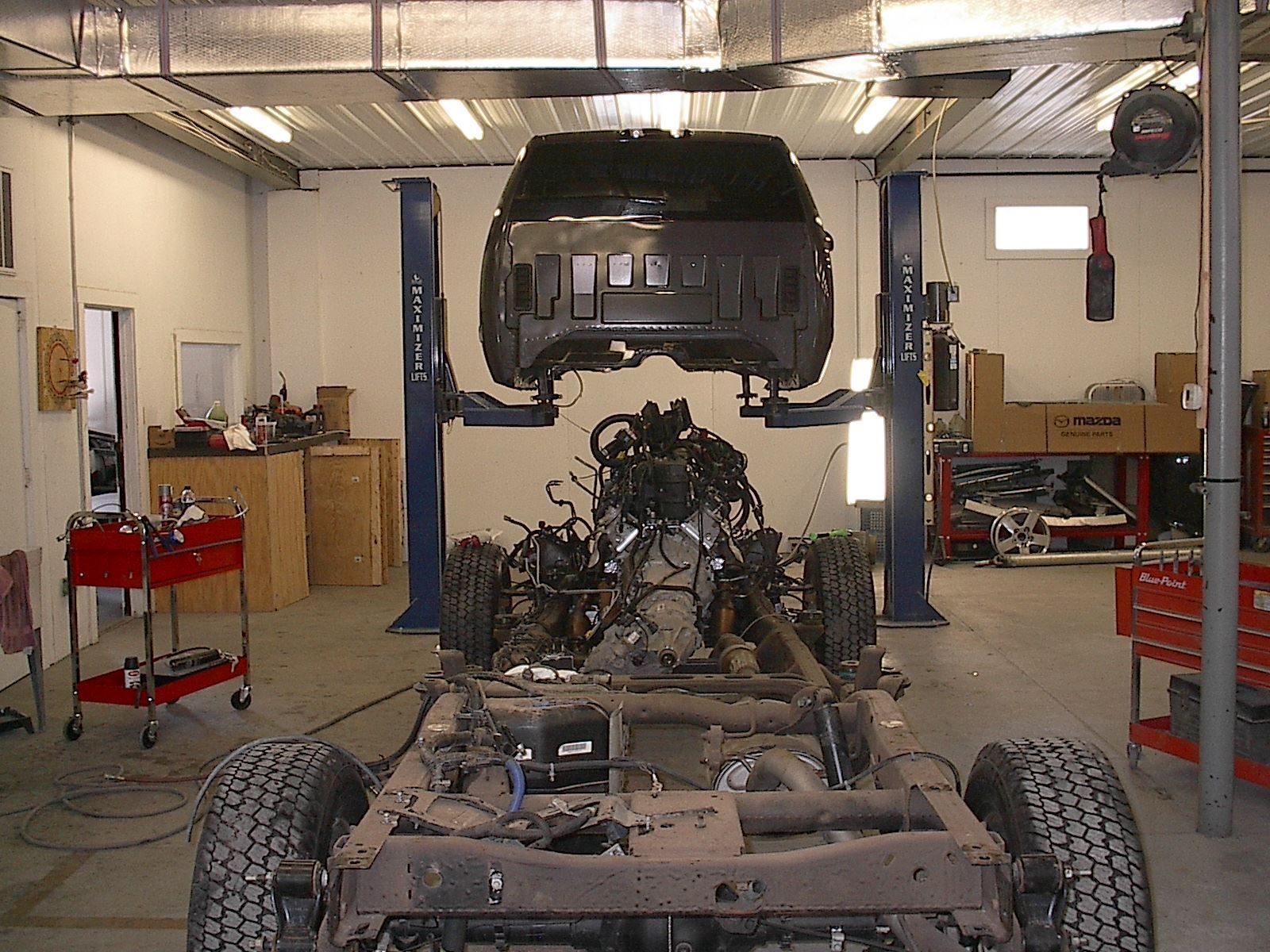 Partially assembled car chassis in an auto repair shop with the hood raised overhead
