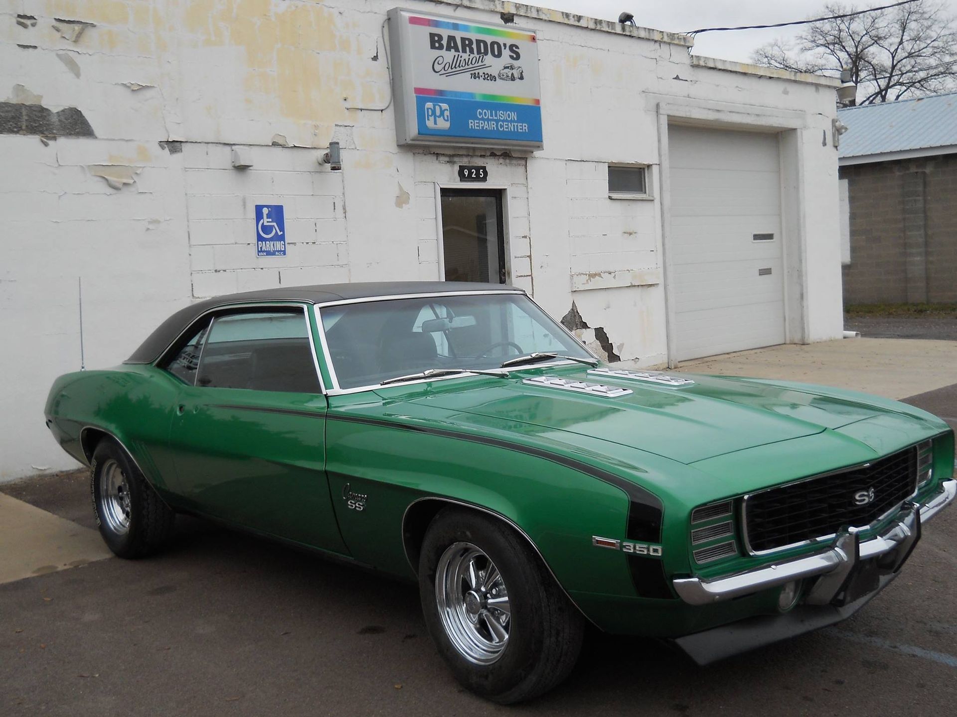 Green classic muscle car parked outside a white garage building.