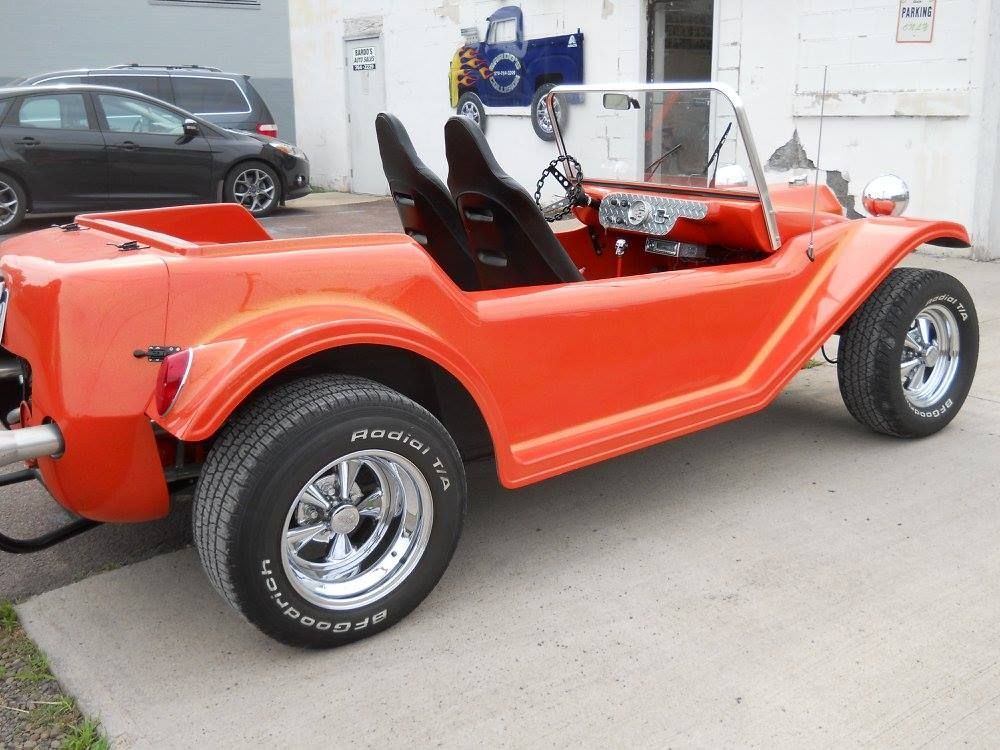 Bright orange dune buggy with black seats parked outdoors on a concrete lot