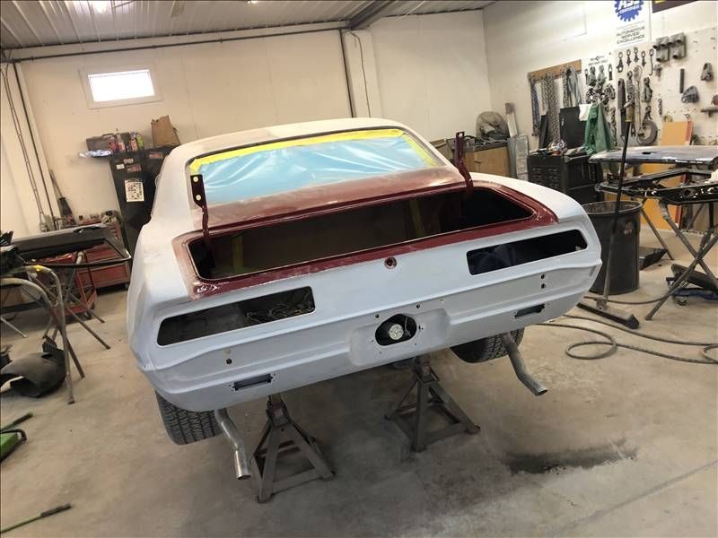 White classic car body in a workshop, raised on jack stands with rear panels open for repair