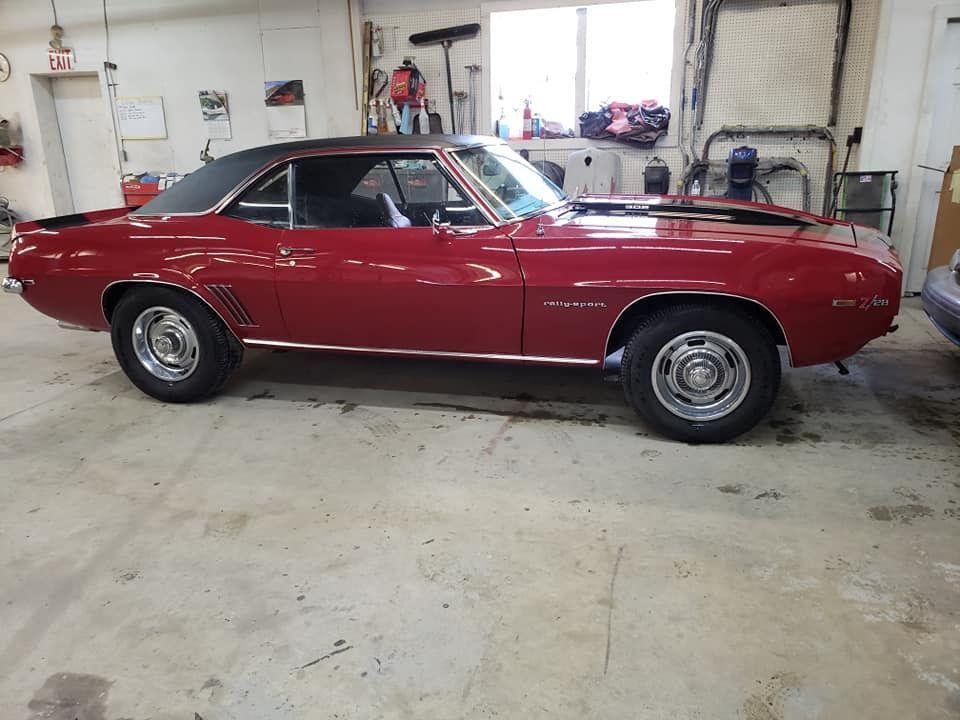 Red classic two-door car parked inside a garage on a concrete floor.