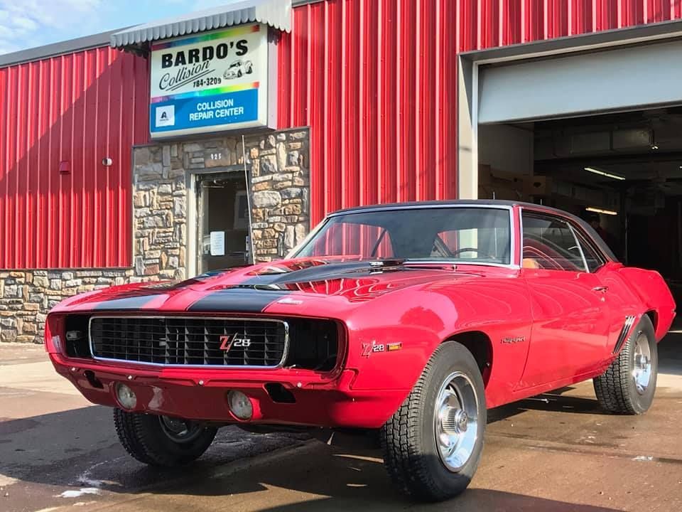 Red classic muscle car parked outside Bardo’s garage on a sunny day