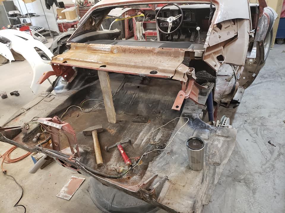 Stripped car interior in a garage, with exposed metal, tools, and unfinished repair work