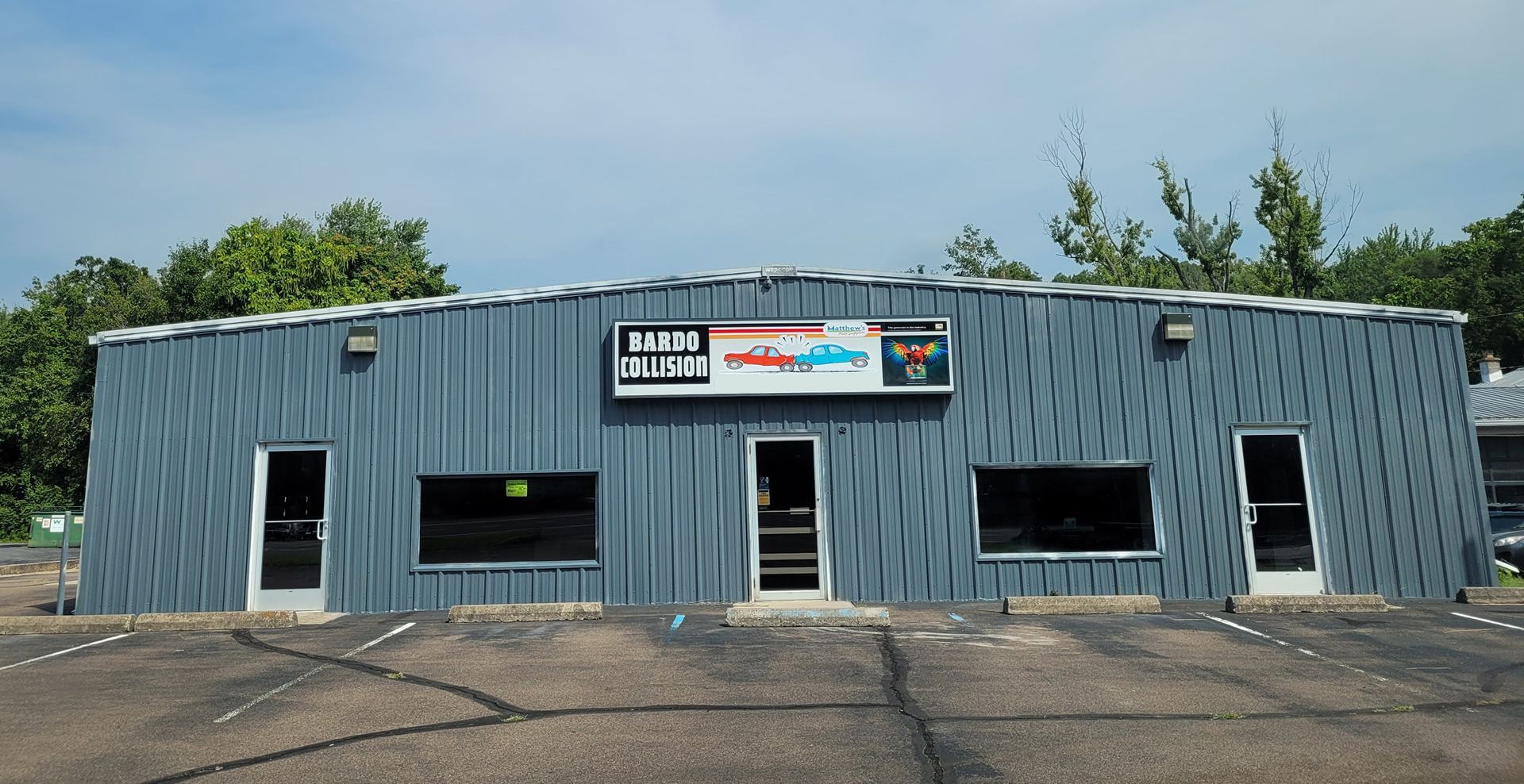 Small blue metal building with a front sign and several windows, seen from across a parking lot.