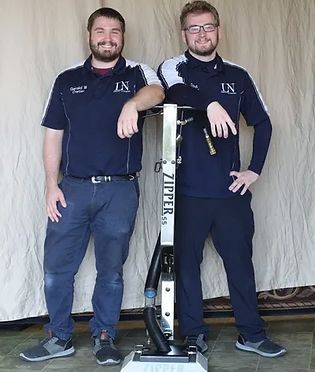 Two men are standing next to each other in front of a zipper vacuum cleaner.