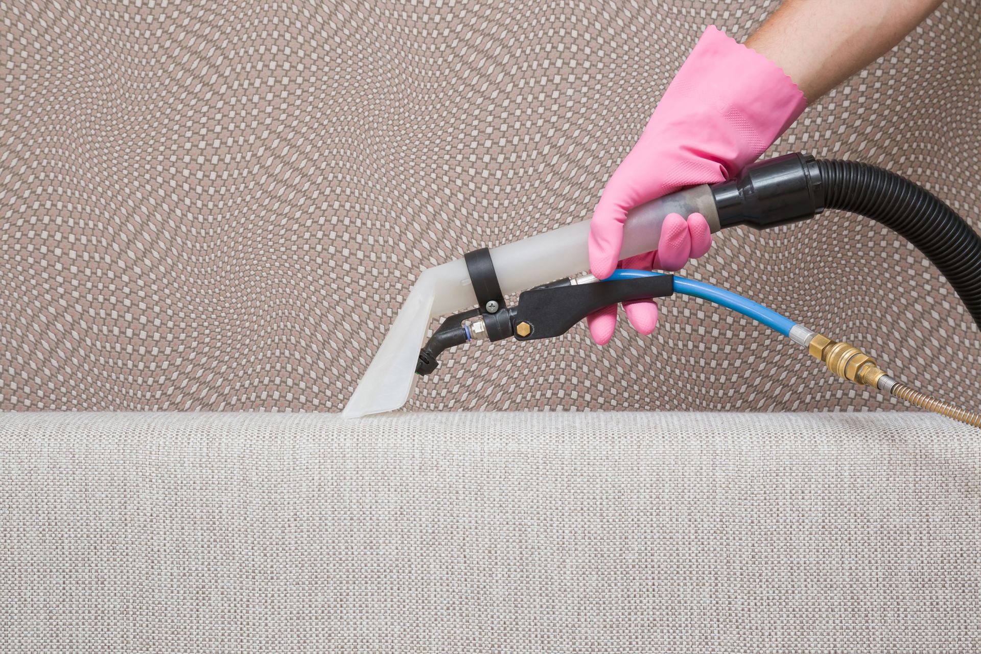 A person is cleaning a couch with a vacuum cleaner.