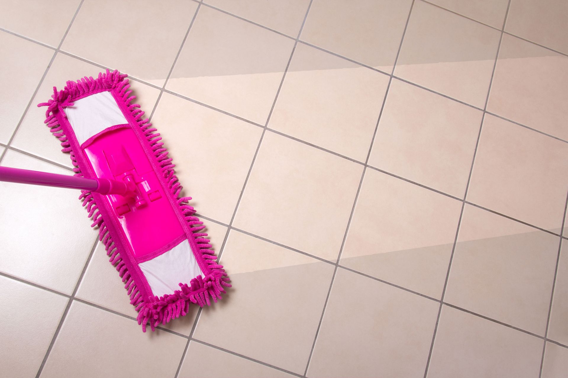 A pink mop is being used to clean a tiled floor.