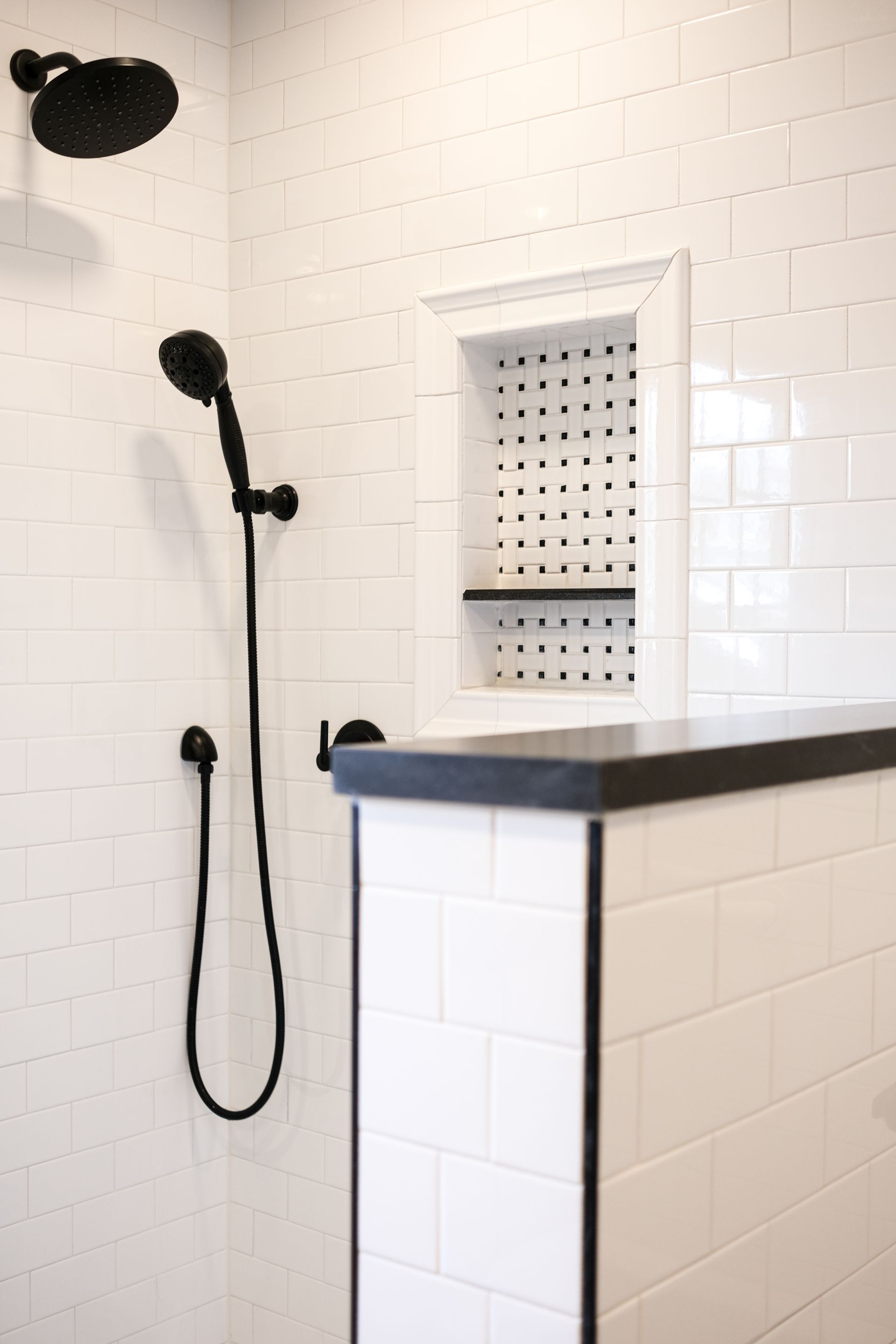 A shower with white subway tiles, black fixtures, and a square-tiled recessed niche with a black shelf.