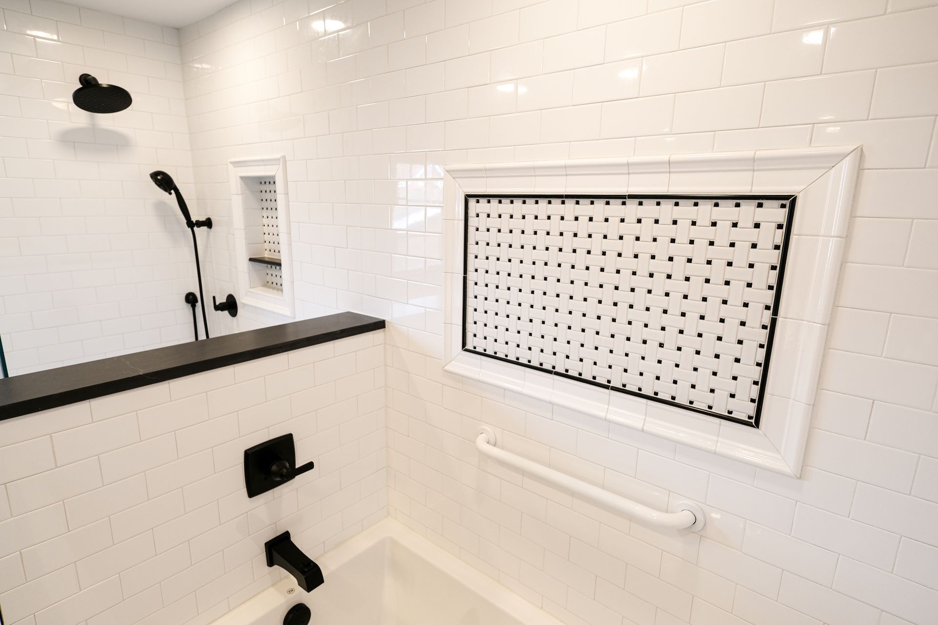 A modern bathroom shower featuring white subway tiles, a black faucet, a built-in shelf, and a horizontal white grab bar.