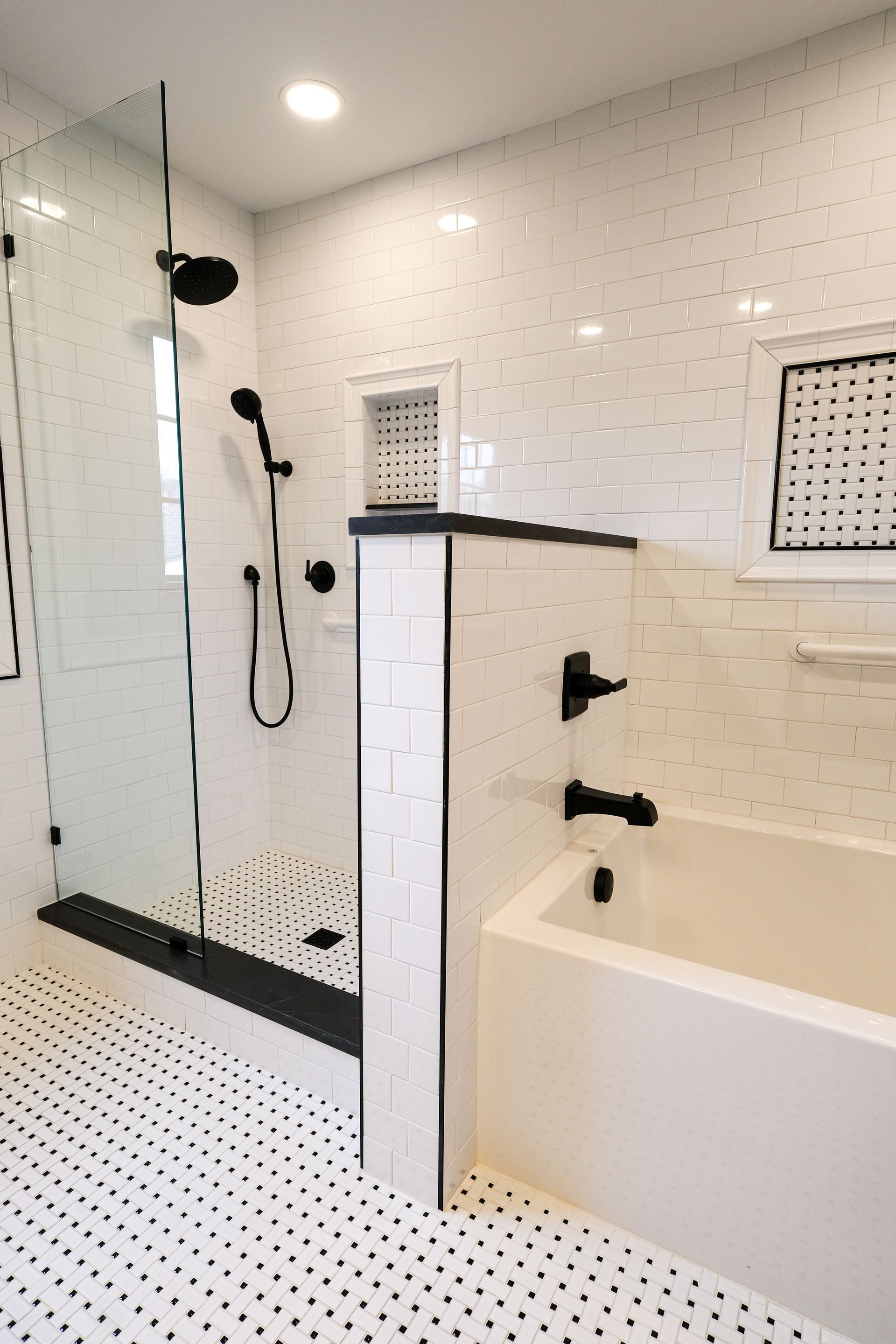 A modern bathroom with a glass-enclosed shower, a white soaking tub, white subway tiles, and black fixtures.