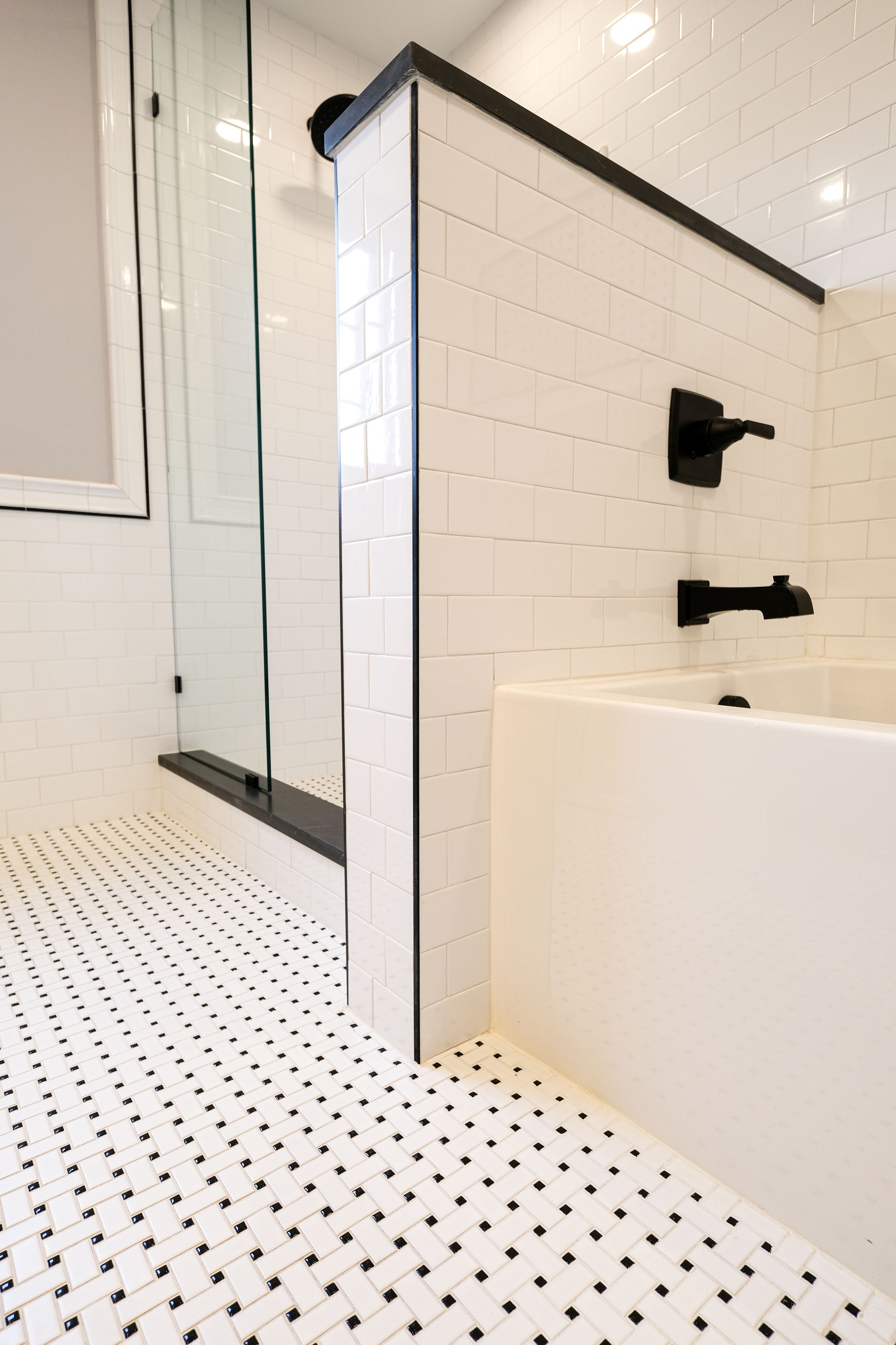 A bathroom interior featuring a white tiled half-wall, a bathtub with matte black fixtures, and a black-and-white tiled floor.