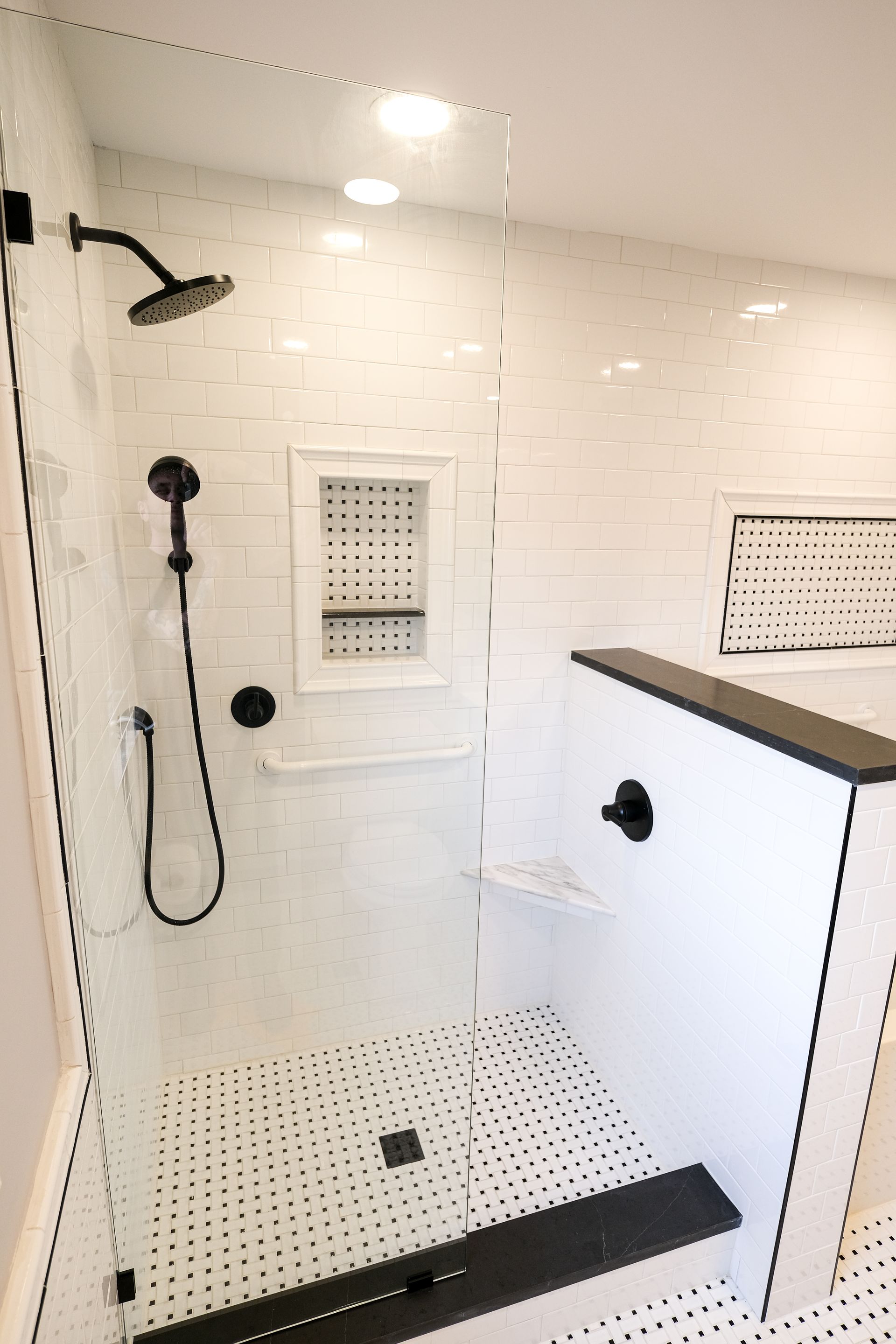 A modern walk-in shower with white subway tile, black fixtures, and a black and white mosaic tiled floor.