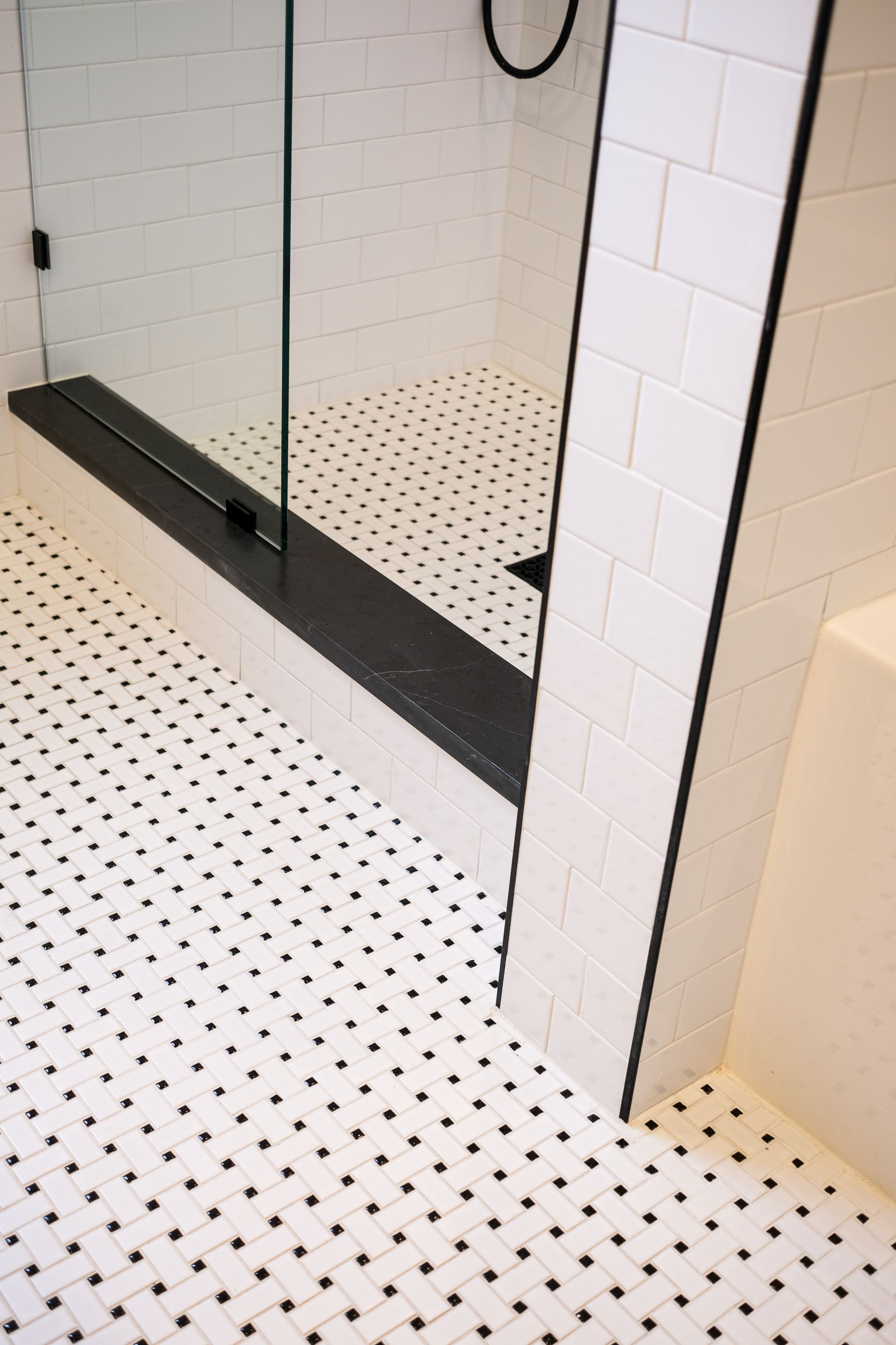 A walk-in shower with a black threshold, white subway-tiled walls, and a white floor with a black grid pattern.