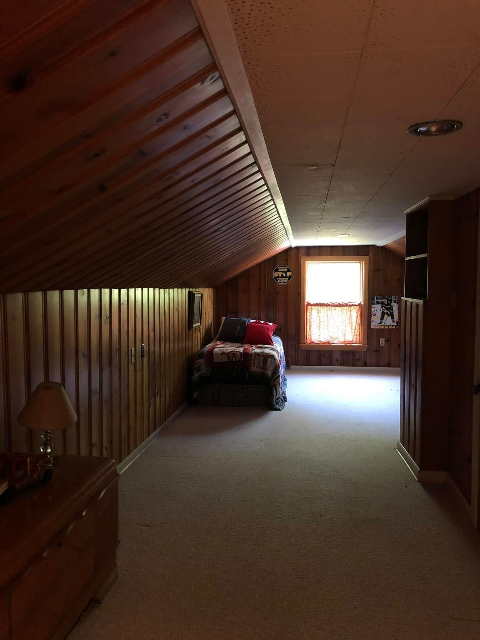 Bedroom with wood paneling, sloped ceiling, and a bed near a window.