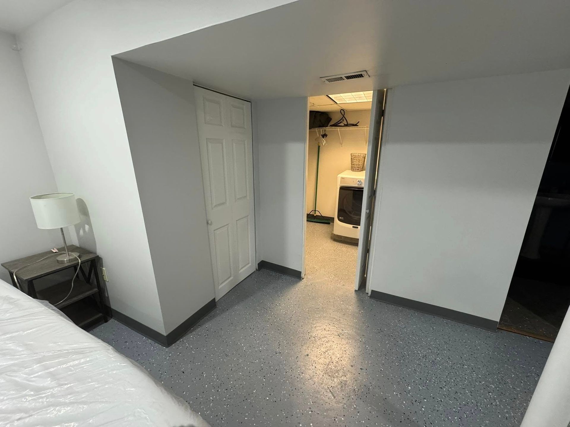 Bedroom with gray floor and white walls. A doorway leads to a laundry area with a washing machine.