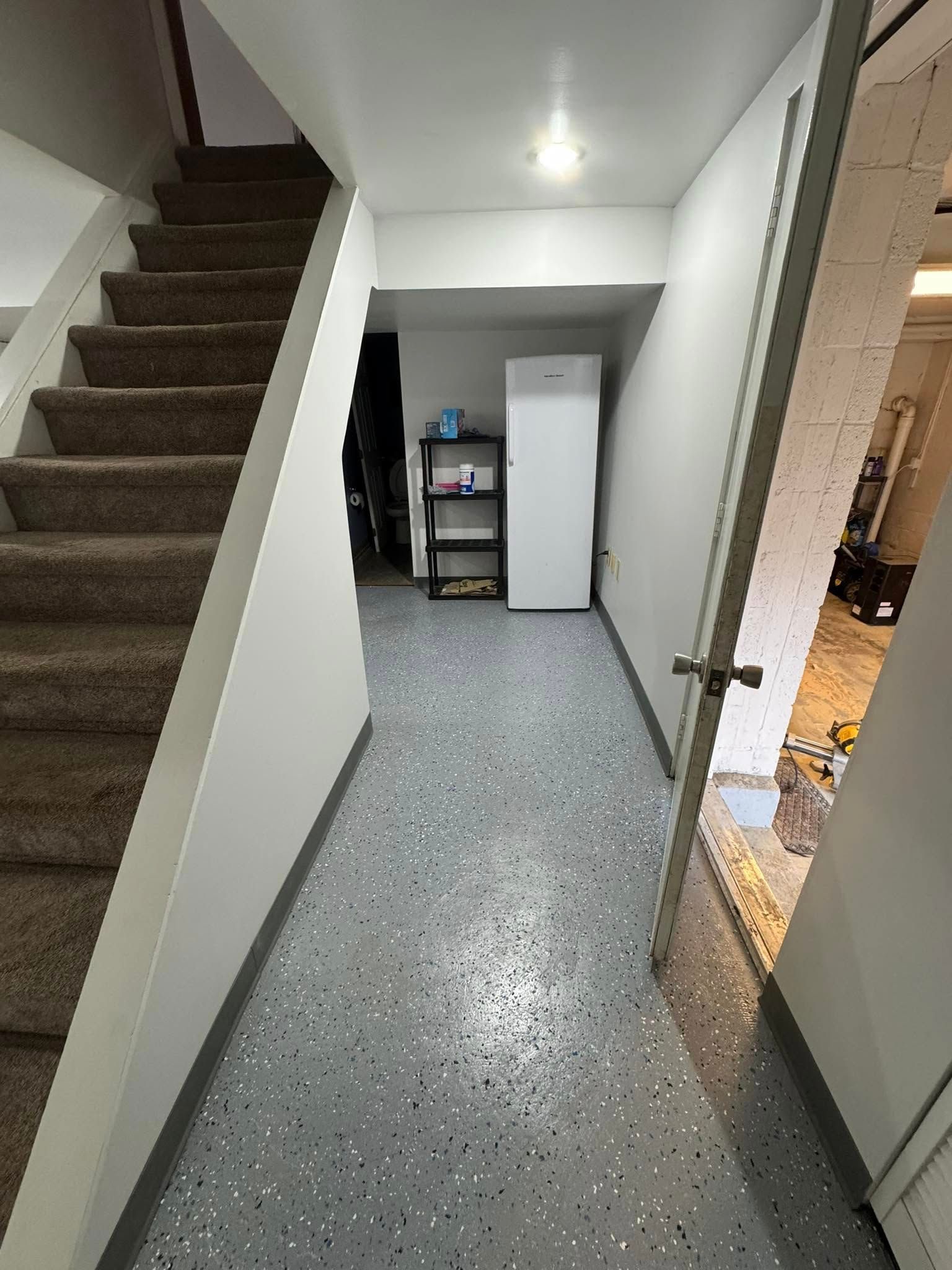 Staircase leads to a hallway with speckled floor and a partially open door to the right. A refrigerator and shelving are visible.