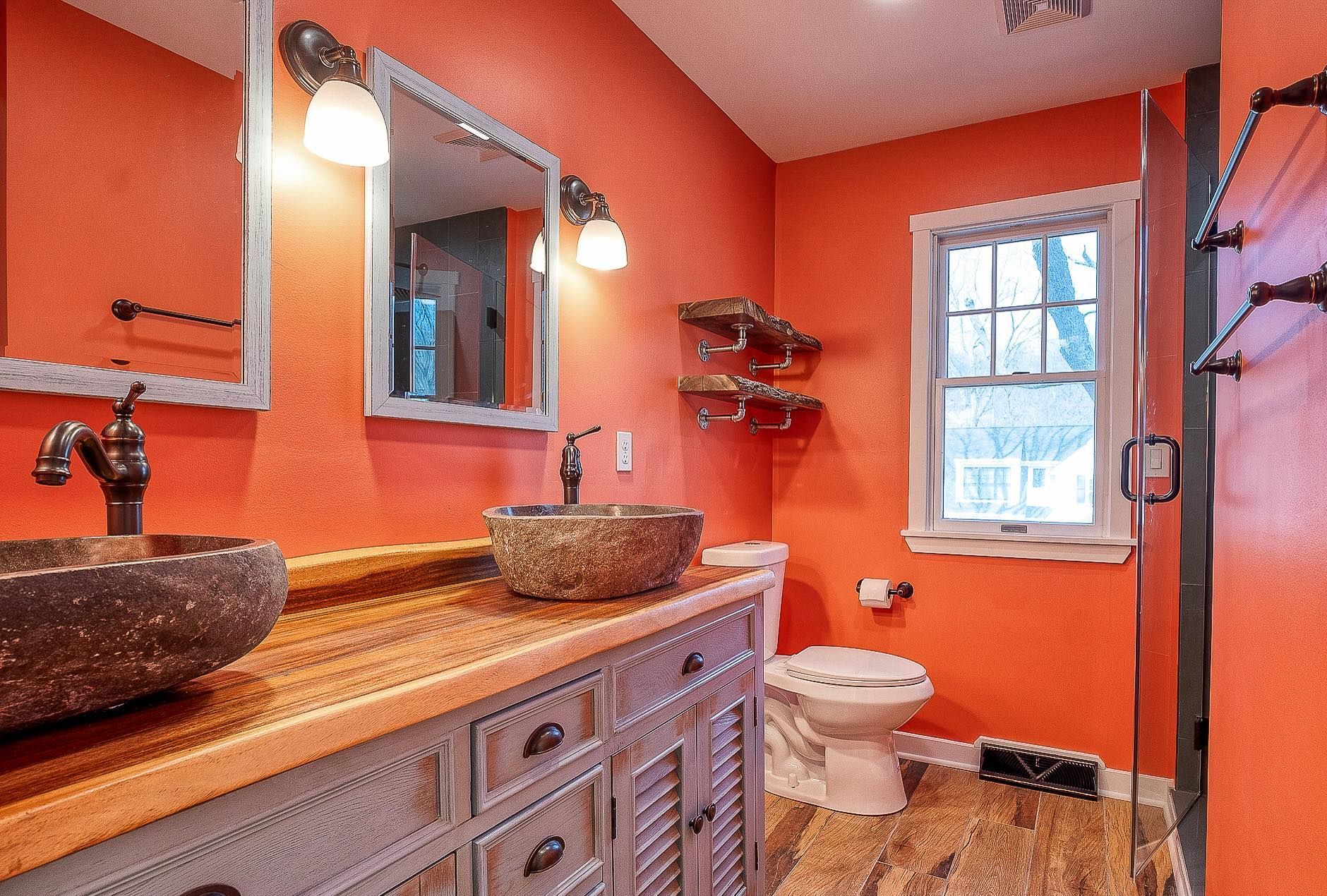 Rustic bathroom with orange walls, stone sinks on a wooden vanity, and a window.