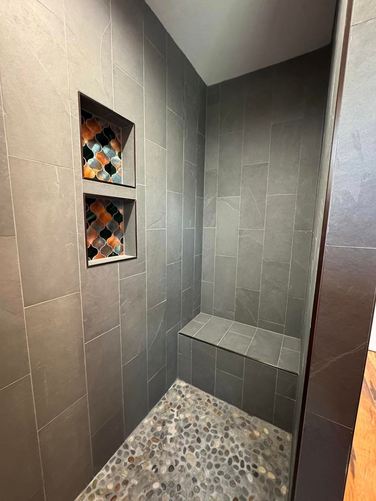 Dark tiled shower with mosaic-tiled niches, pebble floor, built-in bench.