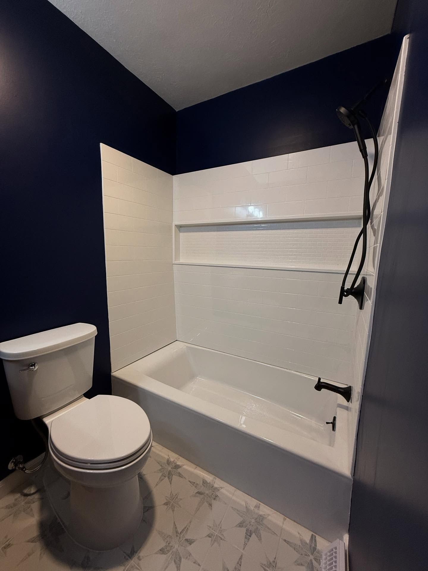 Bathroom with white tub, toilet, and shower surround. Dark blue walls and patterned floor.
