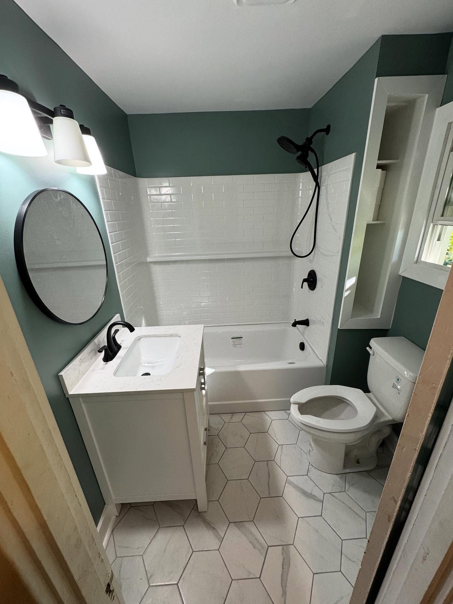 A newly renovated bathroom with white and black accents. Features include a tub, toilet, and vanity with hexagonal floor tiles.